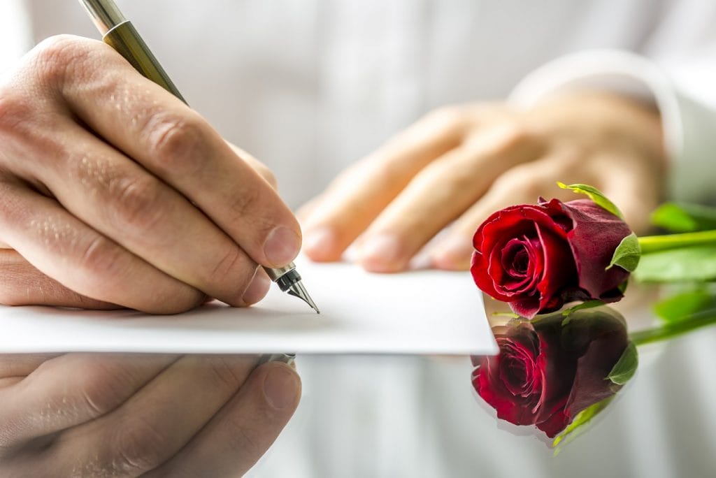 Homme écrivant une lettre à la main avec une rose posée à côté de lui