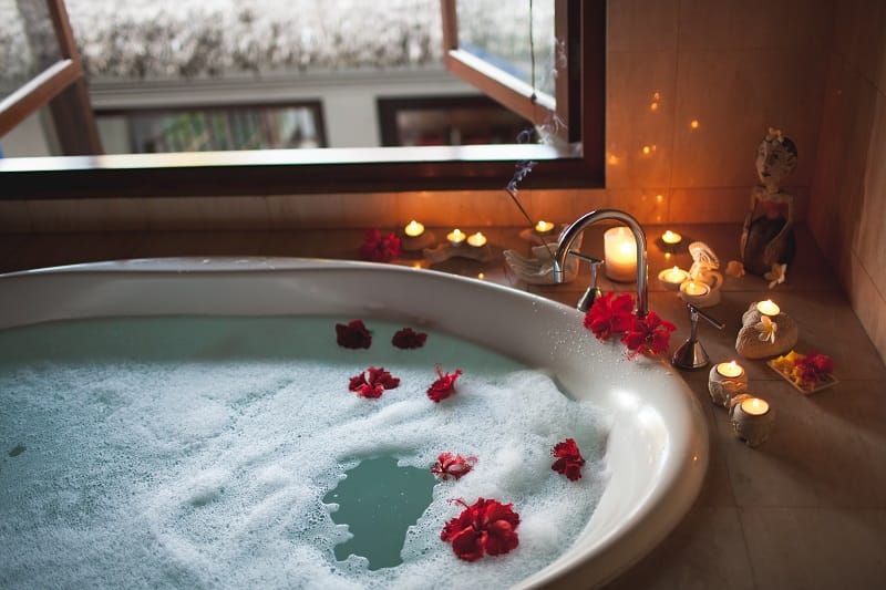 Baignoire remplie d'eau et de mousse avec des fleurs rouges flottantes et des bougies tout autour