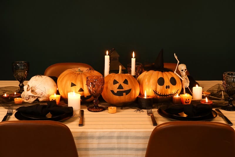 Chemin de table pour Halloween fait de citrouilles, bougies, squelettes et crânes