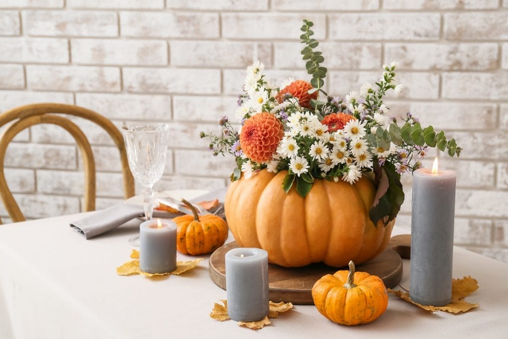 Une table décorée avec des bougies et une citrouille faisant office de vase à fleurs