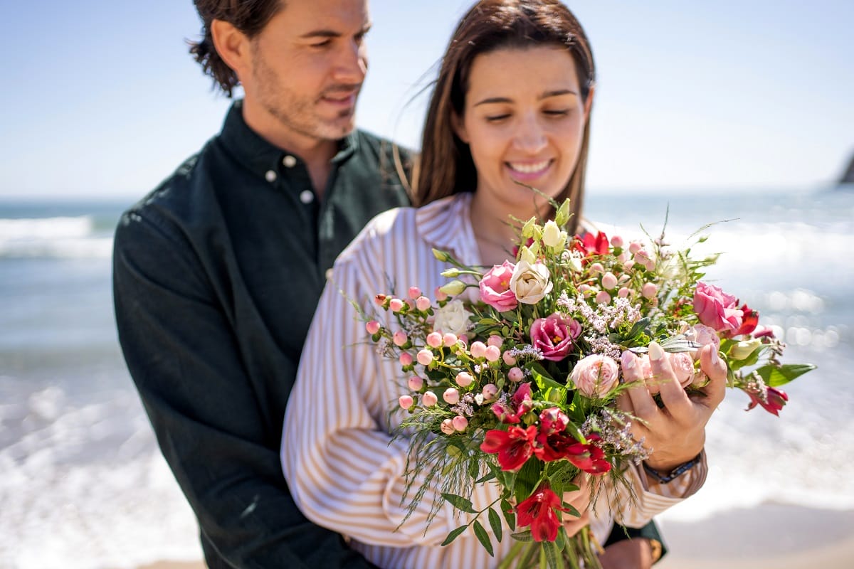 Couple sur la plage tenant un bouquet de fleurs