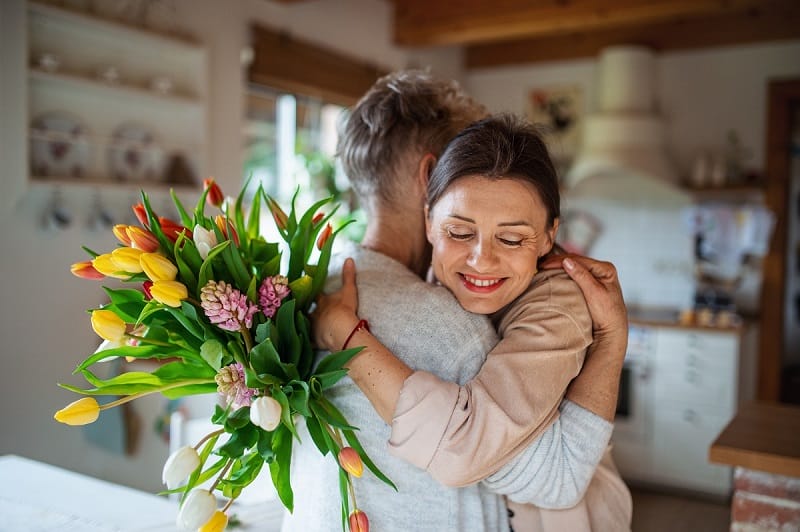 Une mère et sa fille adulte se serrant dans les bras avec un bouquet de fleurs